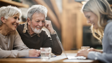 Two retired people talk to a woman working on a laptop